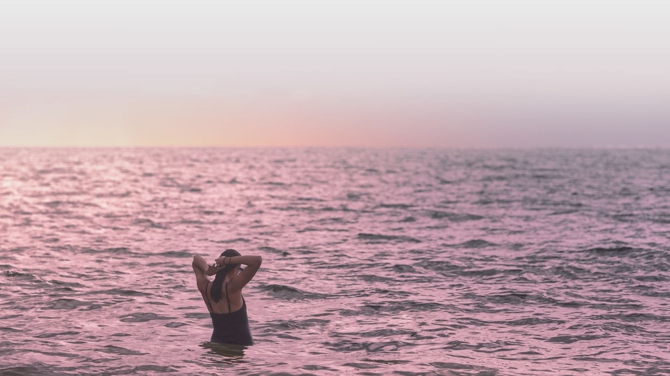 A person wading in the ocean at sunset